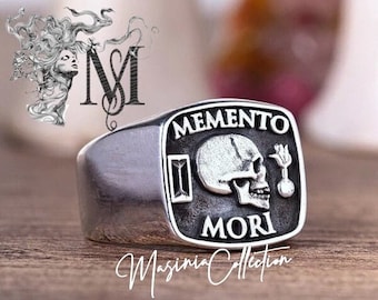 May include: A silver ring with a skull and crossbones design. The ring features the words "Memento Mori" and a Roman numeral II.