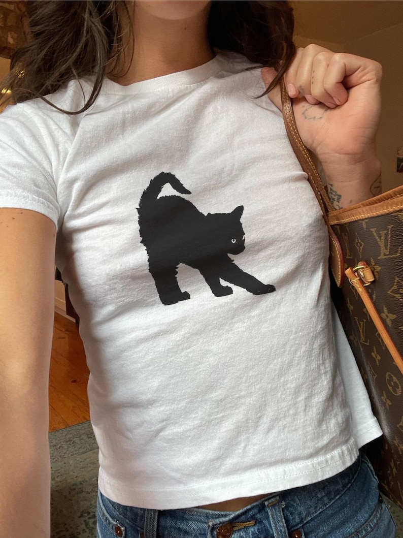 May include: A white t-shirt featuring a black silhouette of a cat on the front.
