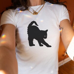 May include: White t-shirt featuring a black silhouette of a cat stretching on the front.