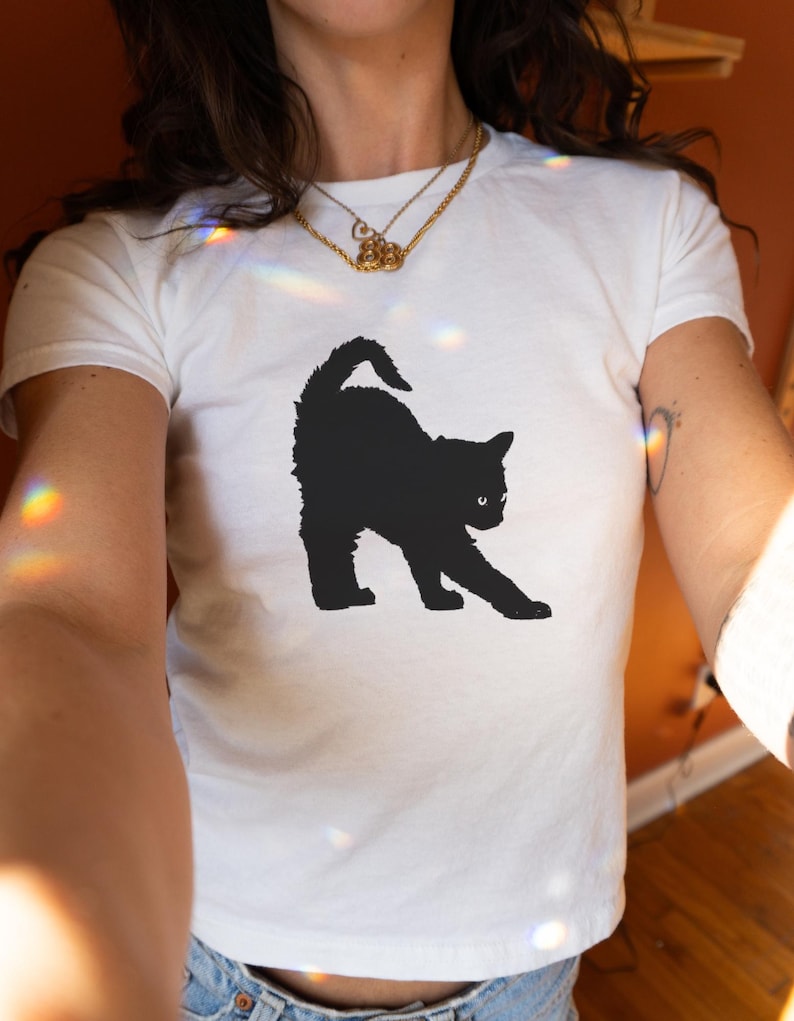 May include: White t-shirt featuring a black silhouette of a cat stretching on the front.