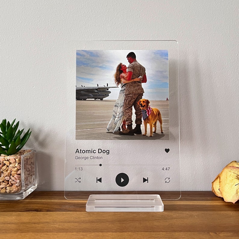 May include: A clear acrylic photo display featuring a couple embracing, a golden retriever wearing a patriotic bandana, and the text "Atomic Dog" by George Clinton. The display includes a stand and a music player interface.