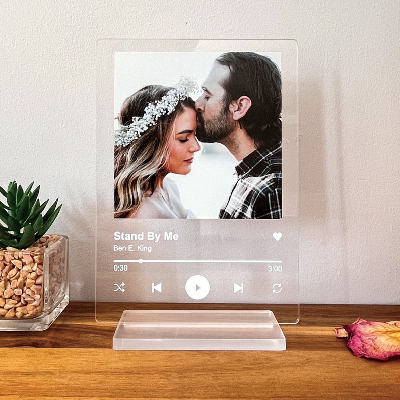 May include: Clear acrylic photo display featuring a couple with the text "Stand By Me" by Ben E. King. The display includes a base and a graphic resembling a music player interface. The photo shows a man kissing a woman's forehead.