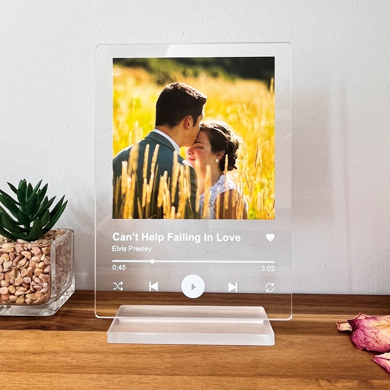 May include: A clear acrylic photo block featuring a couple in a field of tall grass. The text "Can't Help Falling In Love" by Elvis Presley is printed below the photo, along with a music player interface.