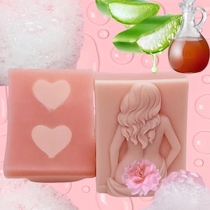 May include: Two pink soaps, one with two heart cutouts, the other with a woman's figure and a pink flower. Aloe vera leaves and a small glass bottle with liquid are also in the image. The background is pink with bubbles.