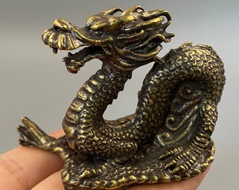 May include: A bronze dragon figurine with intricate details. The dragon is posed in a coiled position, with its head raised and mouth open. The sculpture has a textured surface and a weathered appearance, suggesting an antique or vintage piece. The dragon is a symbol of power and good fortune.