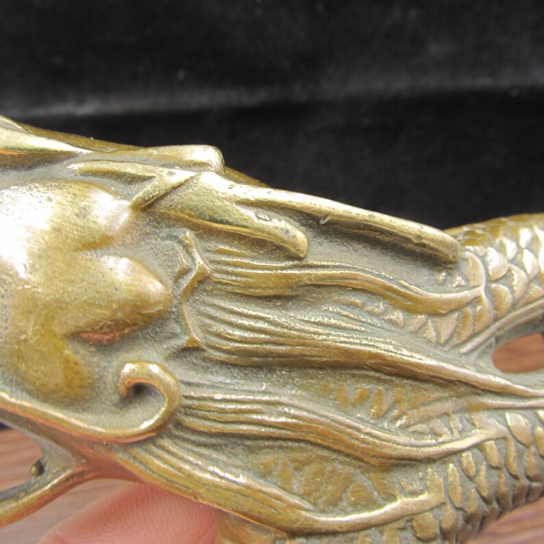 May include: Close-up of a bronze dragon sculpture. The dragon's head is detailed with scales, a flowing mane, and a fierce expression. The sculpture has a weathered appearance, suggesting age and craftsmanship. The dragon's body is partially visible.