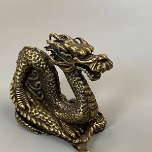 May include: A detailed brass dragon figurine with intricate scales, a detailed head, and a curled body. The dragon is a golden colour and appears to be made of metal. The figurine is a decorative item.
