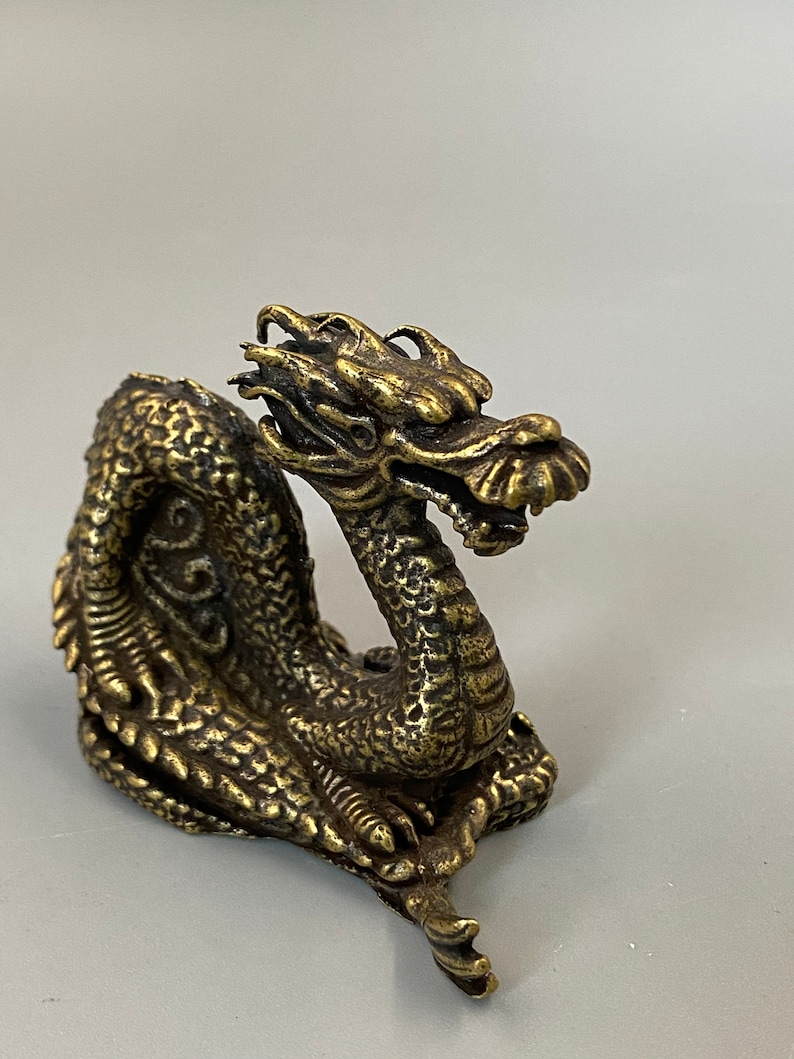 May include: A detailed brass dragon figurine with intricate scales, a detailed head, and a curled body. The dragon is a golden colour and appears to be made of metal. The figurine is a decorative item.