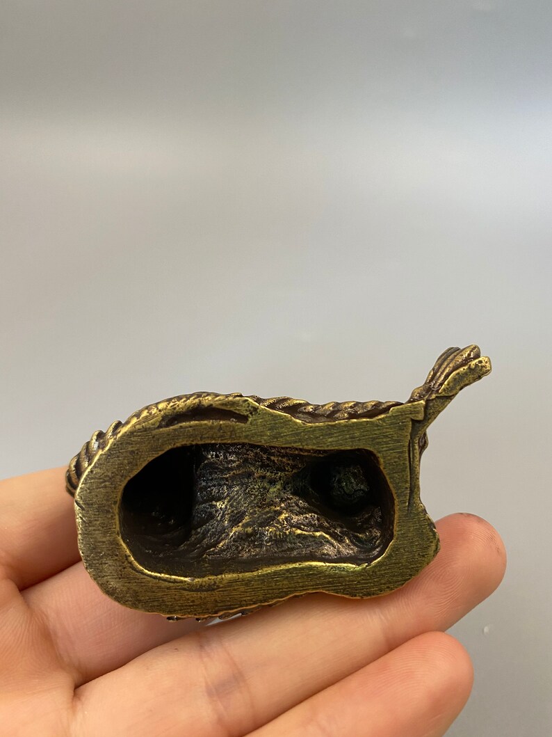 May include: A small, antique-style brass figurine. The figurine has a detailed, textured surface with a dark patina. The object appears to be a religious or decorative item, possibly a small statue or sculpture.