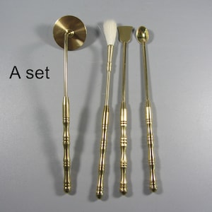 May include: A set of four brass tools, including a round disc on a handle, a brush, a spatula, and a spoon. The tools have decorative handles and are arranged against a gray background. The text "A set" is visible in the image.