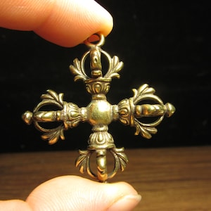 Könnte beinhalten: Ein detaillierter, goldfarbener Anhänger mit kreuzartigem Design. Der Anhänger weist verzierte, symmetrische Muster und eine kleine Schlaufe oben zum Aufhängen auf. Die komplizierten Details und das gealterte Aussehen deuten auf einen Vintage- oder Antik-Stil hin.