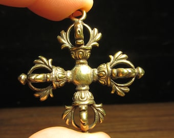 Pode incluir: Um pendente dourado detalhado com um design em forma de cruz. O pendente apresenta padrões ornamentados e simétricos e uma pequena argola no topo para pendurar. Os detalhes intrincados e a aparência envelhecida sugerem um estilo vintage ou antigo.