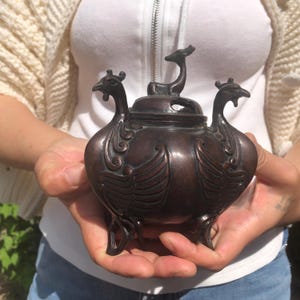 Op de afbeelding: Bronzen wierookbrander met vogelachtige ontwerpen en een hertvormige handgreep. De brander heeft een afgeronde body, gedetailleerde vleugels en drie kleine voetjes. Het deksel heeft een hertfiguur.