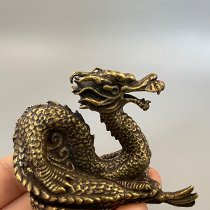 May include: A detailed brass dragon figurine with a textured body and intricate facial features. The dragon is posed in a curved position, with its head raised and mouth open. The figurine has a vintage appearance.