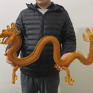 Könnte beinhalten: Goldene Drahtskulptur eines Drachen. Der Drache ist aufwendig gearbeitet mit einem langen, gewundenen Körper, detailliertem Kopf und fließendem Schwanz. Die Skulptur hat eine leuchtend goldene Farbe.