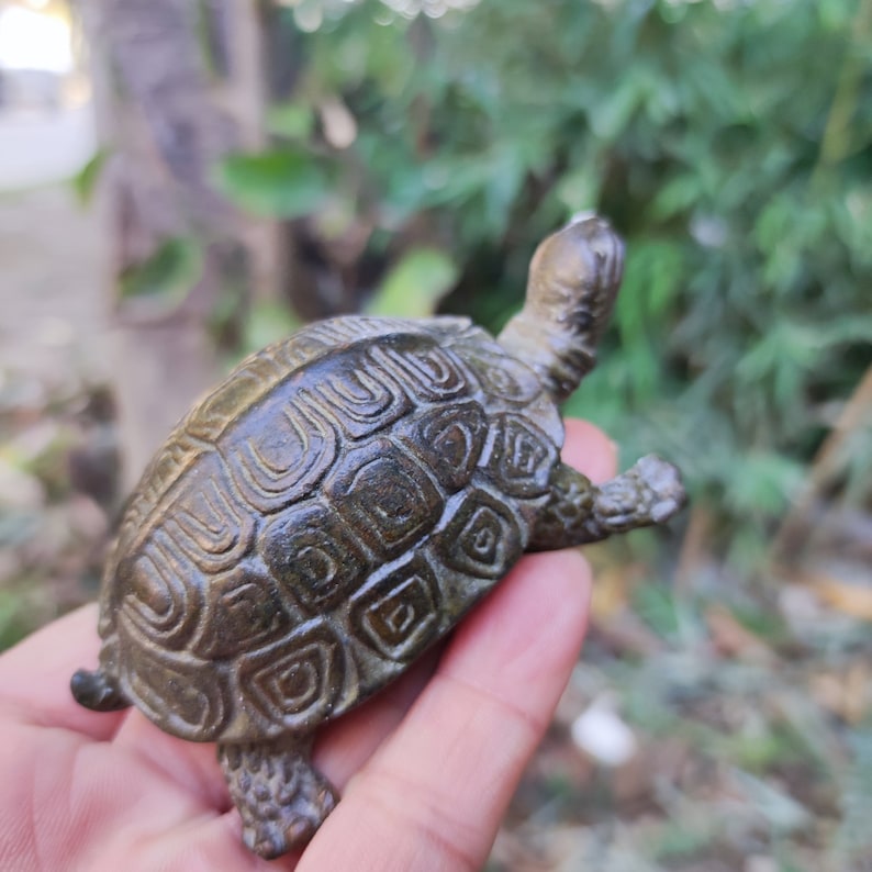 May include: A bronze-colored turtle figurine with detailed shell patterns. The sculpture has a textured surface and is posed with its head and legs extended. The figurine is a decorative item, likely for display.
