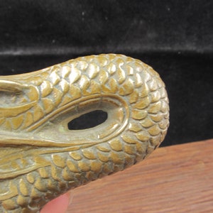 May include: Close-up of a bronze-colored dragon head sculpture. The dragon's head features detailed scales and an open eye. The sculpture is likely made of metal and has a weathered appearance, suggesting it may be an antique or vintage piece.