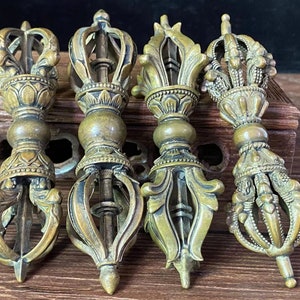 May include: Four antique bronze vajra scepters, each with intricate floral and geometric designs. The vajras are displayed on a wooden surface, showcasing their detailed craftsmanship and historical significance. The scepters vary slightly in their crown and handle designs.