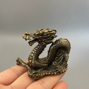 May include: A detailed bronze dragon figurine with intricate scales and a detailed head. The dragon is posed in a coiled position, with its head raised. The figurine is a decorative item, likely for display or collection.