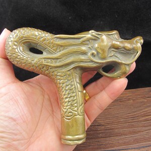 May include: A detailed bronze dragon head cane handle. The handle features a dragon's head with intricate scales and flowing mane. The handle is a warm, antique gold color.
