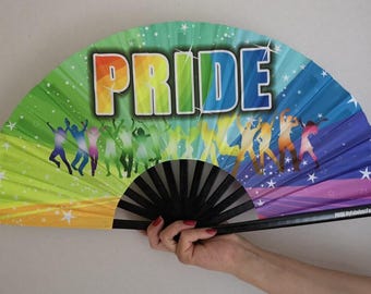 May include: A rainbow-colored Pride fan with the word "PRIDE" in large, colorful letters. The fan features silhouettes of dancing figures and stars. The fan is held open, displaying its full design.