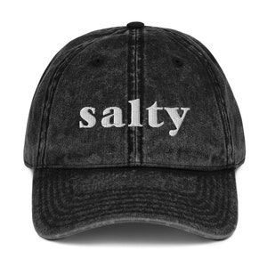 May include: A black vintage washed cotton baseball cap with white embroidered text that reads "salty".