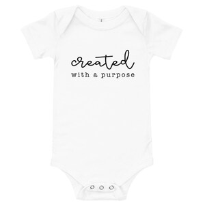 Puede incluir: Un body blanco para bebé con texto negro que dice "created with a purpose".