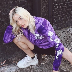 May include: A purple tie-dye long-sleeved shirt with the text "We Rave Hard" and mushroom graphics on the sleeves.