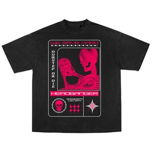 May include: Black t-shirt featuring a pink graphic of a skeleton holding a skull. The graphic includes the text "WE RAVE HARD", "DUBSTEP OR DIE", and "HEADBANGER".