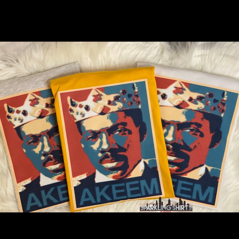 Pu&ograve; includere: Tre magliette con una grafica di un uomo con una corona, con il nome "AKEEM" stampato sotto. La grafica &egrave; nei toni del rosso, blu e beige. Le magliette sono grigie, gialle e bianche. Il marchio "Sparkling Shirts of Atlanta" &egrave; in basso.