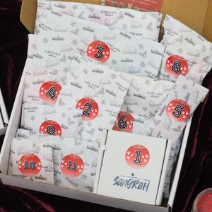 May include: A white box with a white and red pattern containing 11 numbered packages. The packages are labelled with numbers 1 through 11. The box is open and the packages are visible. The box is labelled "Sangrah".