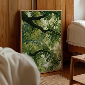 Op de afbeelding: Een rechthoekige wandkunstprint in een lichthouten lijst met een kikkerperspectief op een dicht bladerdak. De afbeelding toont donkerbruine boomtakken die zich over het frame uitstrekken, bedekt met felgroene bladeren tegen een lichte lucht.