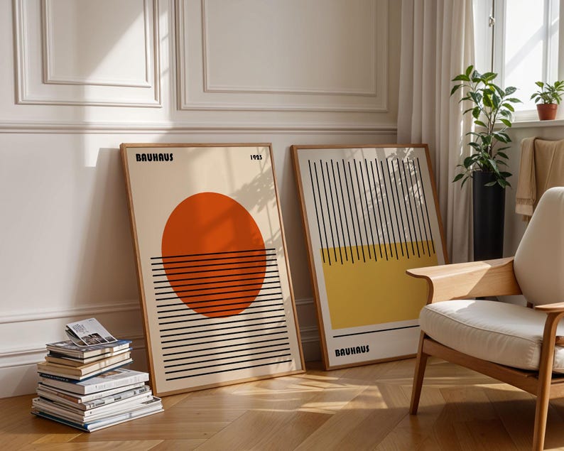 two framed artworks with abstract designs, placed on a wooden floor in a room with a chair and a stack of books.