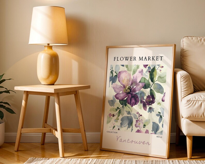 a wooden table with a lamp on top, a framed poster of a flower market, and a beige armchair in the background.