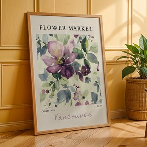 a framed poster of a floral design, placed on a wooden floor next to a potted plant.