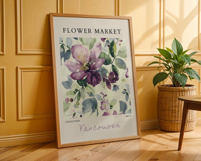 a framed poster of a floral design, placed on a wooden floor next to a potted plant.