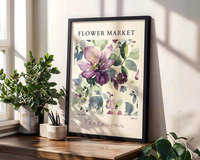 a framed poster of a watercolor painting of a purple flower, placed on a wooden shelf next to potted plants and a small white bowl.