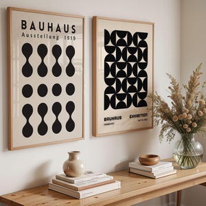 Pode incluir: Dois cartazes emoldurados da exposição Bauhaus. O cartaz esquerdo tem formas pretas e o texto "BAUHAUS Ausstellung 1919". O cartaz direito tem um design geométrico a preto e branco.