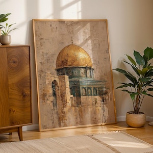 May include: Large framed artwork of the Dome of the Rock in Jerusalem. The painting shows a golden dome and teal details against a textured, neutral backdrop. The artwork leans against a wall near a wooden cabinet and potted plants.