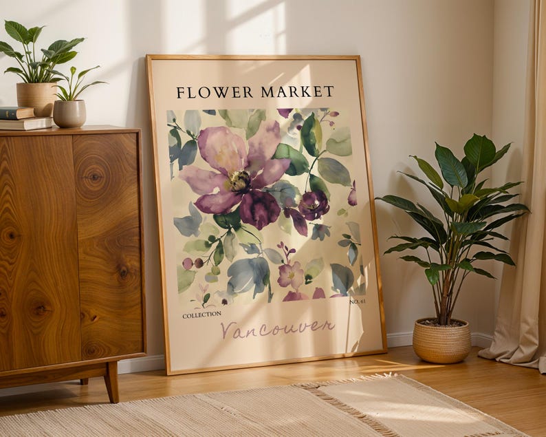 a large framed poster of a floral design, with the text "FLOWER MARKET" and "VANCOUVER" printed on it. The poster is displayed on a wooden cabinet, with a potted plant to the right and a rug on the floor in front of it.