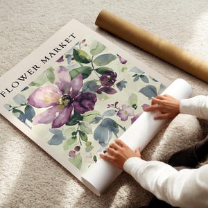 A person is placing a large poster with a floral design on a carpeted floor.