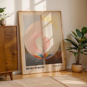Puede incluir: Una lámina artística enmarcada titulada The Dove, No. 1 de Hilma af Klint, que presenta un gran círculo central con un corazón rosa, una línea en espiral vertical y una base de colores del arcoíris, con texto negro en la parte inferior.