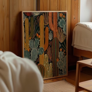 May include: A rectangular framed wall art print featuring a dense, stylised illustration of various cacti and succulents. The artwork uses a dark background with warm tones of orange, yellow, and muted green to depict tall saguaro and prickly pear cacti.