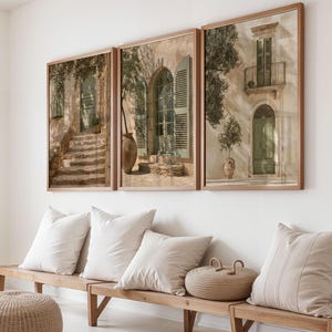 Könnte beinhalten: Drei gerahmte Wandbilder mit mediterraner Architektur, Steintreppen, Bogentüren, grünen Fensterläden und Topfpflanzen. Die Bilder in hellen Holzrahmen hängen über einer Holzbank mit beigen Kissen.