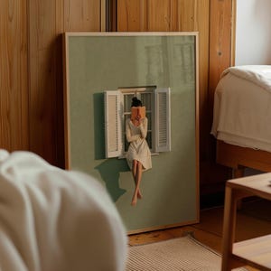 以下が含まれることがあります： セージグリーンの背景に、中央の白い窓枠と開いた鎧戸が描かれた額装アートプリント。クリーム色のドレスを着た人物が窓枠に座り、開いた本を顔の前に持っている様子が表現されています。