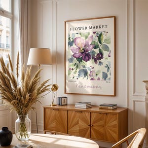 a living room with a large floral print hanging on the wall, a wooden cabinet, a vase with dried flowers, and a lamp on a side table.