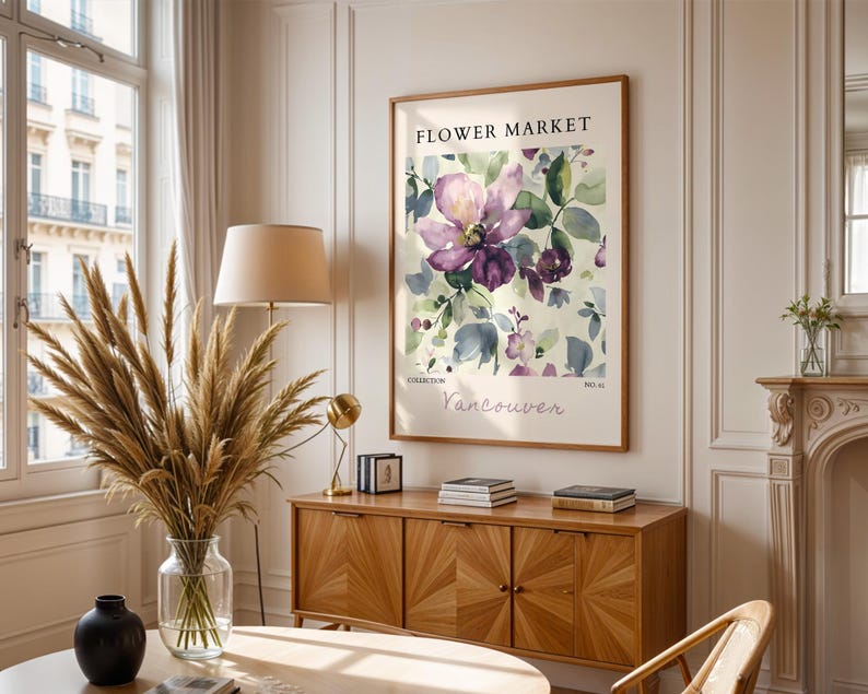 a living room with a large floral print hanging on the wall, a wooden cabinet, a vase with dried flowers, and a lamp on a side table.