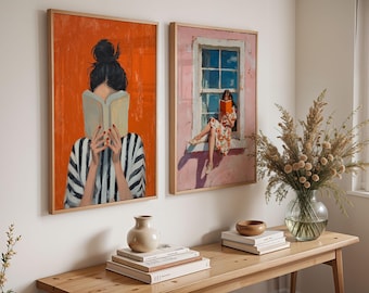 May include: Two framed wall art prints featuring illustrations of people reading books. The left print shows a person with a dark bun holding a book against an orange background. The right print depicts a person sitting in a window frame reading.