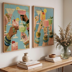 May include: Two rectangular wall art prints in light wood frames featuring a vibrant illustration of multiple hands raised in a toast, holding various colorful cocktails with garnishes like cherries and lemon slices against a bright blue background.