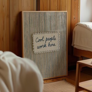 May include: A rectangular framed wall art piece featuring a vertical blue pinstripe pattern on a light background. Centered on the print is a white, scalloped-edge rectangular plaque with the dark blue text Cool people work here.